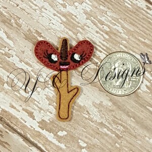 Op de afbeelding: Een vilt applique van een rode en bruine cartoon bloem met een grillig gezicht en wimpers. De bloem zit op een bruine stok.