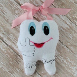 May include: A white plush tooth with a smiling face and a thumbs up gesture. The tooth has blue eyes, a pink mouth, and a pink ribbon attached to the top.