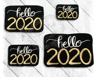 Puede incluir: Cuatro parches de fieltro negro con bordados blancos y dorados. Los parches dicen "hello 2020".