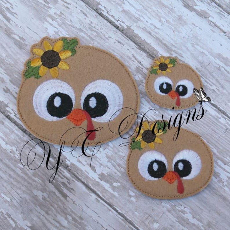 May include: Three felt turkey head appliques with big eyes, a red wattle, and a sunflower on top. The appliques are different sizes.