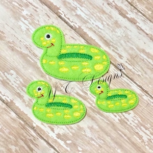 May include: Three green felt appliques shaped like inflatable pool floats with yellow polka dots and green eyes. The floats are in the shape of a duck.