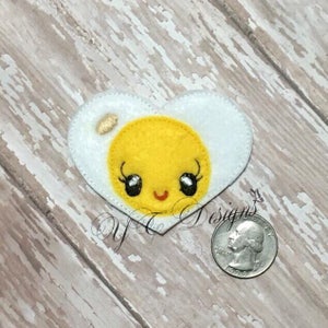 May include: A white felt heart-shaped appliqu&eacute; with a yellow felt yolk inside. The yolk has a smiling face with black eyes and eyelashes.