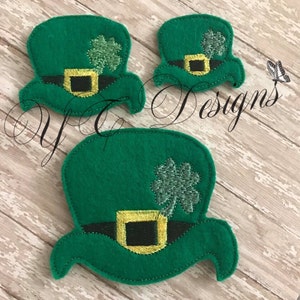 May include: Three felt green leprechaun hats with black and yellow trim and a green shamrock on top. The hats are different sizes.