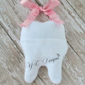 May include: White felt tooth with a pink ribbon tied around the top. The tooth has the text "Y&T Designs" embroidered on the front.