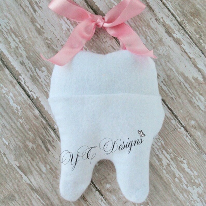 May include: White felt tooth with a pink ribbon tied around the top. The tooth has the text "Y&T Designs" embroidered on the front.