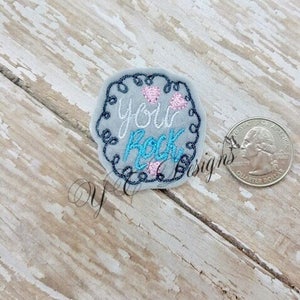 May include: A grey embroidered patch with a white swirl border. The patch says "You Rock" in blue and pink lettering with three pink hearts.