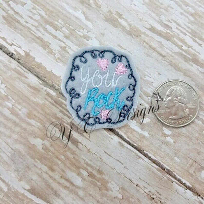 May include: A grey embroidered patch with a white swirl border. The patch says "You Rock" in blue and pink lettering with three pink hearts.