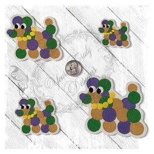 May include: Four embroidered patches of a poodle made of circles in green, purple, gold and brown colors. The patches are on a white wooden background.