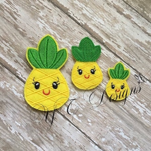 May include: Three embroidered felt pineapple patches with smiling faces. The pineapples are yellow with green tops and are different sizes.
