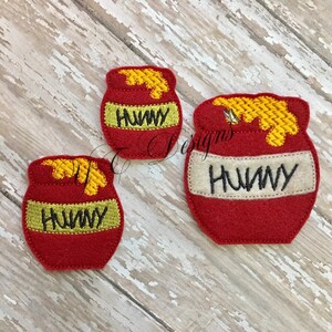 May include: Three felt honey pot appliques in different sizes. The pots are red with yellow honey and the word "Hunny" written in black on a white band.