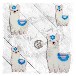 Puede incluir: Cuatro aplicaciones de llama de fieltro blanco con flecos azules y rosas. Cada llama tiene una flor azul en la cabeza y ojos bordados.
