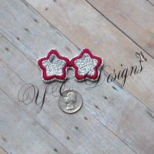 May include: Star-shaped sunglasses with a red border and silver glitter filling. The sunglasses are placed on a wooden surface next to a quarter. The text "yC designs" is visible in the image.