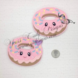 May include: Two pink felt donut patches with brown icing and colorful sprinkles. Each donut has a smiling face with black eyes and a pink mouth.