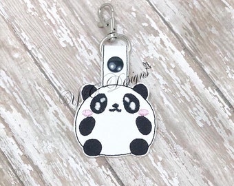 May include: A white and black panda bear keychain with a silver clip. The panda has black eyes and pink cheeks.