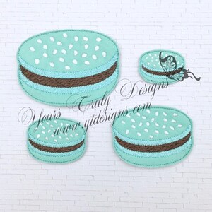 Peut inclure: Quatre macarons bleu sarcelle et marron avec des pépites blanches. Les macarons sont de tailles différentes. Le plus grand macaron est au centre de l'image. Le plus petit macaron est dans le coin supérieur droit de l'image.