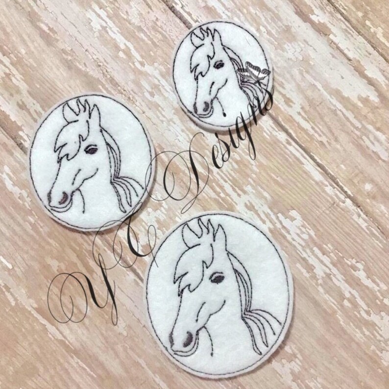 Puede incluir: Tres c&iacute;rculos de fieltro blanco con dise&ntilde;os de cabeza de caballo bordados en negro. Las cabezas de caballo est&aacute;n mirando hacia el lado derecho de la imagen.