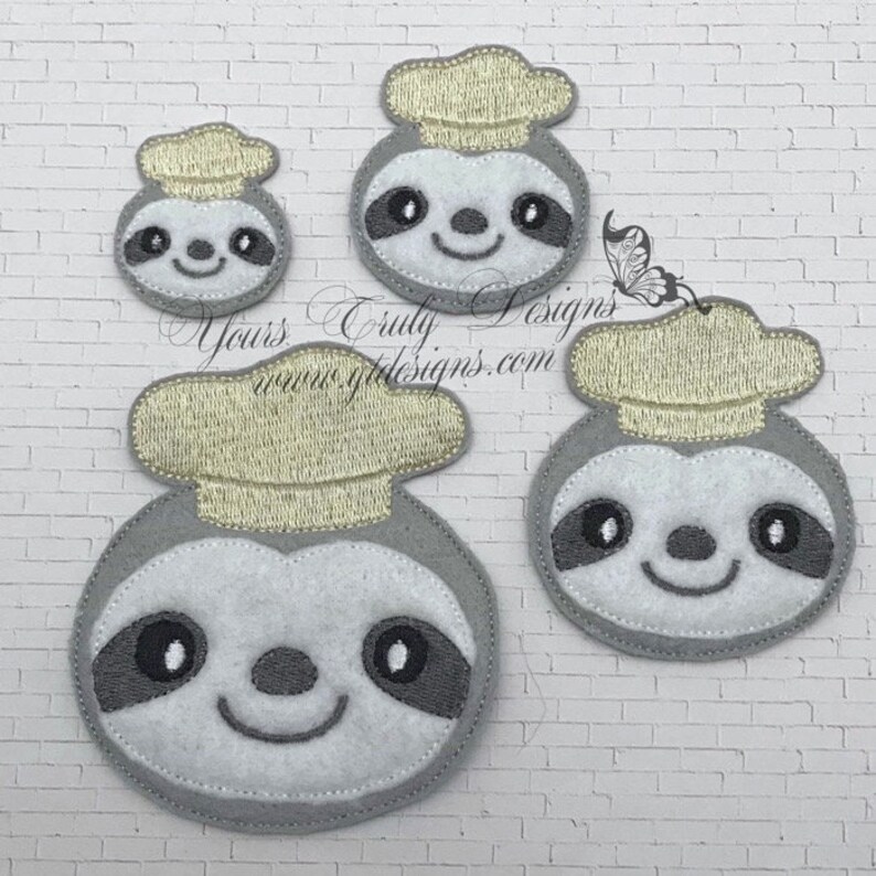 Puede incluir: Tres aplicaciones de fieltro de perezosos con gorros de chef. Los perezosos son grises con ojos negros y una cara blanca. Los sombreros son amarillos. Los perezosos son de diferentes tama&ntilde;os.