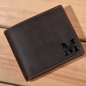 Może przedstawiać: Brązowy sk&oacute;rzany portfel z personalizowanym monogramem. Monogram to duża litera "M" z wygrawerowanym poniżej imieniem "Charlie".