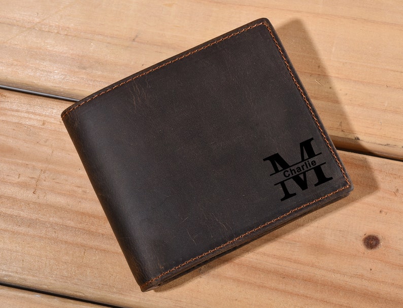 Może przedstawiać: Brązowy sk&oacute;rzany portfel z personalizowanym monogramem. Monogram to duża litera "M" z wygrawerowanym poniżej imieniem "Charlie".