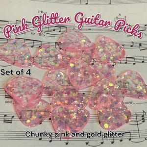 May include: A set of four pink guitar picks with chunky pink and gold glitter. The picks are shaped like teardrops and are scattered on a sheet of music. The text "Pink Glitter Guitar Picks" is at the top.