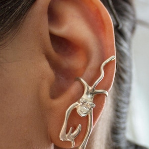 Può includere: Orecchino a clip in argento a forma di scimmia con un solo diamante sul petto. La scimmia è appollaiata sull'orecchio con le braccia e le gambe distese.