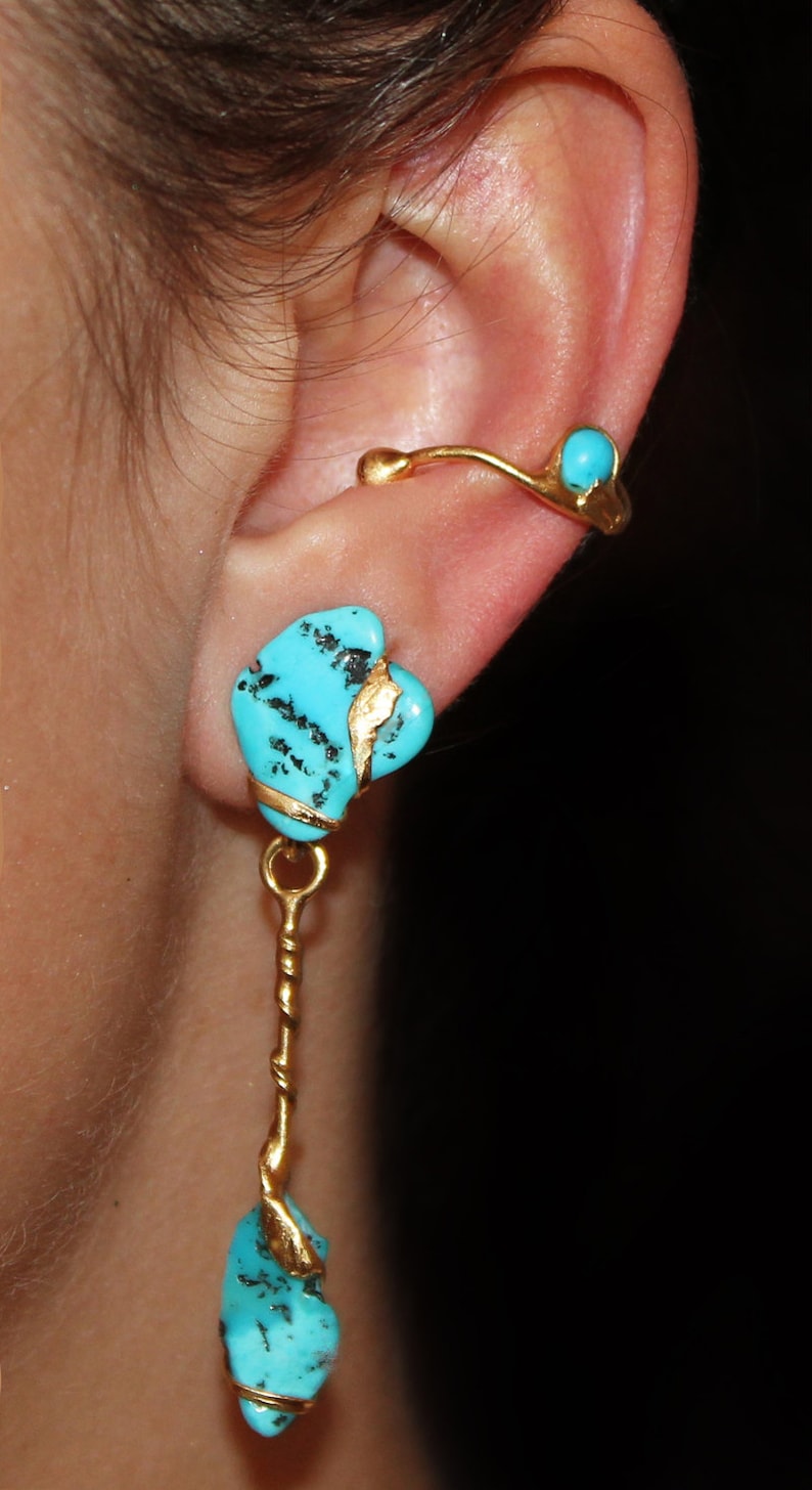 May include: Turquoise and gold earrings with a dangling turquoise stone. The earrings are made of gold and feature a turquoise stone with gold accents.