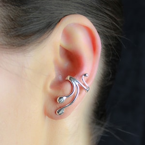 May include: Silver ear cuff with a curved, abstract design. The cuff is worn on the upper part of the ear.