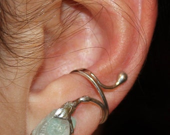 May include: A silver ear cuff with a light blue gemstone. The cuff is shaped like a curved branch with a small ball at the end.