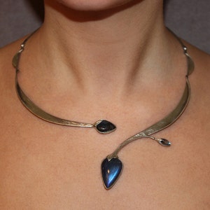May include: A silver statement necklace with a curved design and a dangling blue gemstone pendant.