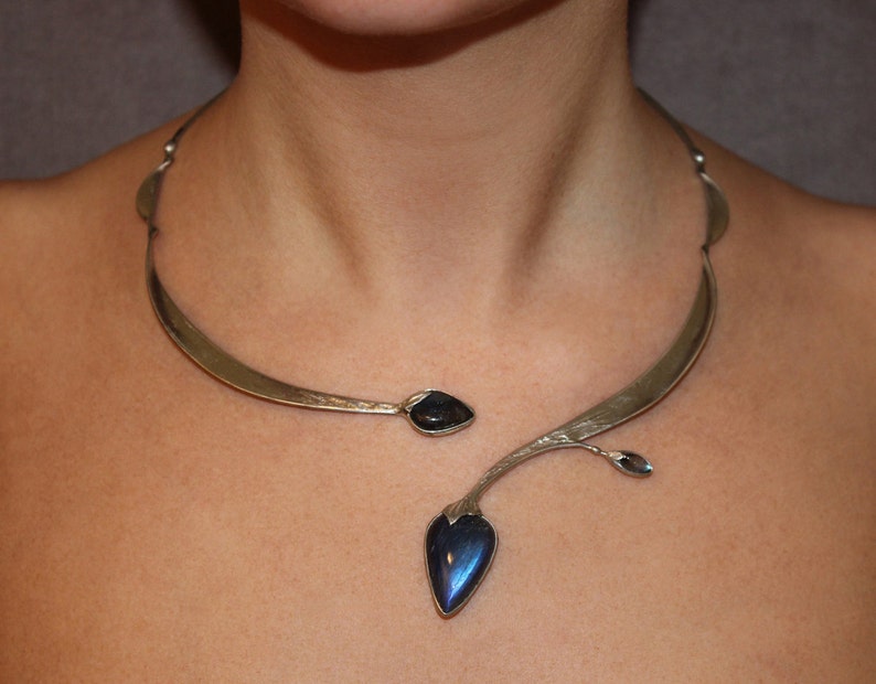 May include: A silver statement necklace with a curved design and a dangling blue gemstone pendant.