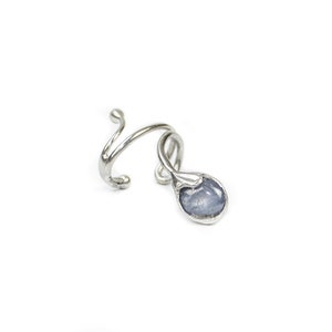 May include: A silver-toned ring with a swirling design and a teardrop-shaped, light blue gemstone. The ring has an open design, with the gemstone suspended from the band.