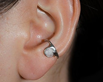 May include: A silver ear cuff with a white stone. The cuff is designed to wrap around the upper part of the ear.