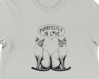May include: A light gray t-shirt with a black and white illustration of two cats sitting back to back. A speech bubble above the cats says "Purrfectly in Love".
