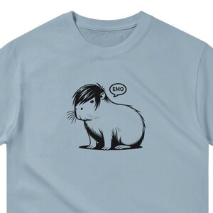 May include: Light blue t-shirt with a black and white illustration of a capybara with an emo hairstyle and a speech bubble that says "EMO".