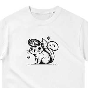 Puede incluir: Camiseta blanca con una ilustración en blanco y negro de una ardilla con un peinado humano. La ardilla sostiene un globo de diálogo que dice "NUTS".