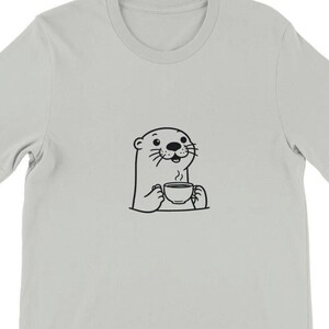 Könnte beinhalten: Ein hellgraues T-Shirt mit einer schwarz-weißen Illustration eines Otters, der eine Tasse Kaffee hält.