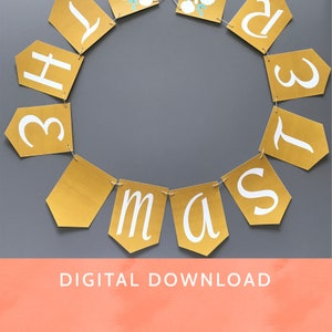 Op de afbeelding: Een gouden banner met witte letters die "Kerstmis" spellen met bloemmotieven. De banner hangt op een grijze achtergrond. De tekst "DIGITAAL DOWNLOADEN" staat onderaan de afbeelding.
