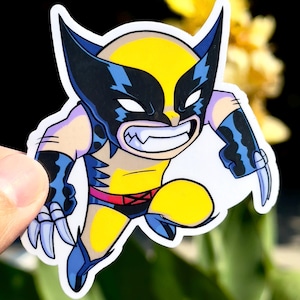 May include: A cartoon sticker of Wolverine in a dynamic pose. The character is depicted with a yellow and black mask, blue and yellow costume, and silver claws. The sticker is held by a hand against a blurred background.