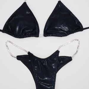 Puede incluir: Bikini negro con adornos de cristal. La parte superior es de estilo triangular con una tira halter y la parte inferior es de corte atrevido.