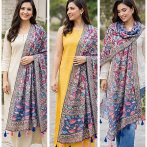 Puede incluir: Dupatta de algod&oacute;n y semi-lino con estampado Kalamkari. La imagen muestra a tres mujeres con coloridas bufandas. Las bufandas tienen un borde azul con un dise&ntilde;o floral en rosa, azul y verde. Las bufandas tienen borlas en los extremos.