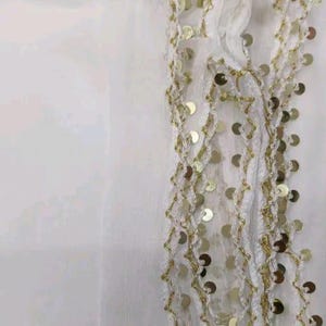 May include: White fabric with gold sequin and thread embellishments. The design features a zig-zag pattern with attached gold sequins. The fabric appears to be a sheer material, with the embellishments adding texture and visual interest.