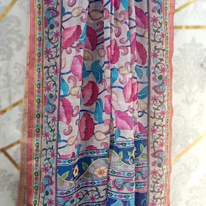 Puede incluir: Bufanda estampada con motivos florales en rosa, azul y verde. La bufanda presenta un dise&ntilde;o repetido de flores y hojas estilizadas sobre un fondo claro. Los bordes est&aacute;n ribeteados y adornados con borlas.