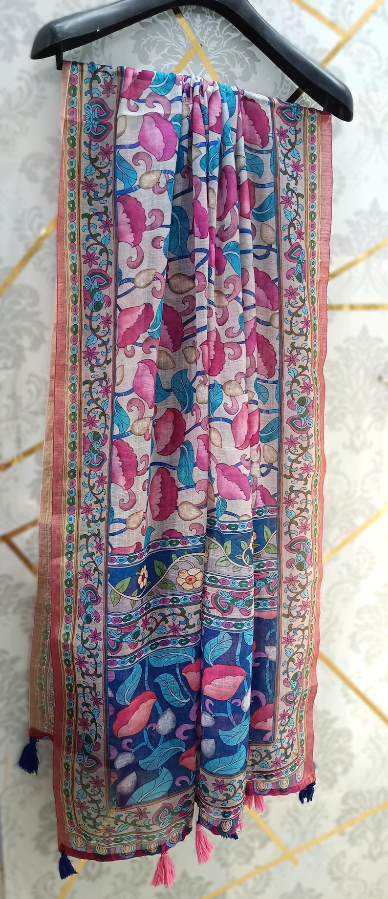 Puede incluir: Bufanda estampada con motivos florales en rosa, azul y verde. La bufanda presenta un dise&ntilde;o repetido de flores y hojas estilizadas sobre un fondo claro. Los bordes est&aacute;n ribeteados y adornados con borlas.