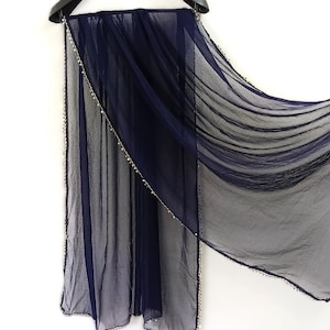 May include: A sheer navy blue scarf with a delicate beaded trim along the edges. The scarf is draped over a black hanger, showcasing its flowing, lightweight fabric. The scarf's design is simple and elegant.