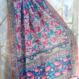 Puede incluir: Bufanda estampada con motivos florales en tonos rosa, azul y beige. El dise&ntilde;o presenta flores y hojas estilizadas, con un borde azul oscuro y borlas en los extremos. La bufanda est&aacute; colgada de una percha negra.