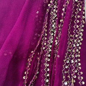 May include: A vibrant magenta fabric with gold sequin embellishments. The fabric is draped, showcasing its texture and the intricate detailing of the gold sequins. The design suggests a garment or decorative textile.