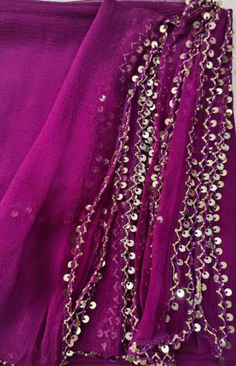 May include: A vibrant magenta fabric with gold sequin embellishments. The fabric is draped, showcasing its texture and the intricate detailing of the gold sequins. The design suggests a garment or decorative textile.