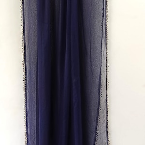 May include: A navy blue sheer scarf with a delicate, beaded trim. The scarf is hanging on a black hanger against a white background. The fabric appears lightweight and flowing, suitable for various occasions.