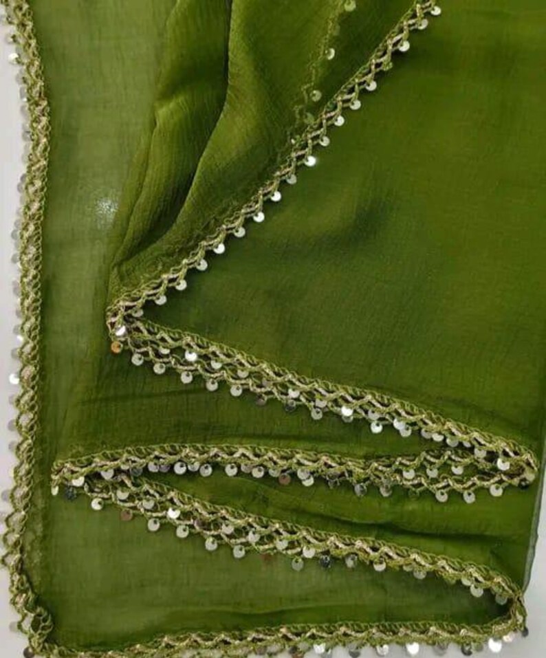 May include: Olive green fabric with a delicate, shimmering trim. The trim is a light gold color and is adorned with small, round sequins. The fabric is draped, creating soft folds and shadows. The overall effect is elegant and refined.