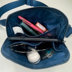 Interior of bag is lined and has 2 open, pockets. Picture shows navy bag, opened with mascara, a pen, and lip gloss in one pocket. A phone in the center compartment, and sunglasses, ear buds, and hand sanitizer in the other pocket.